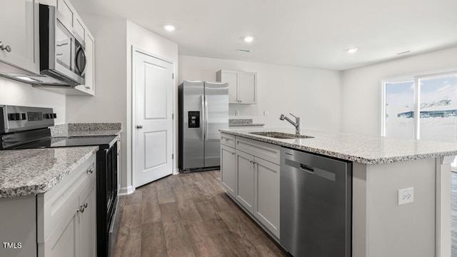 kitchen with a sink, dark wood-type flooring, light stone counters, stainless steel appliances, and a kitchen island with sink