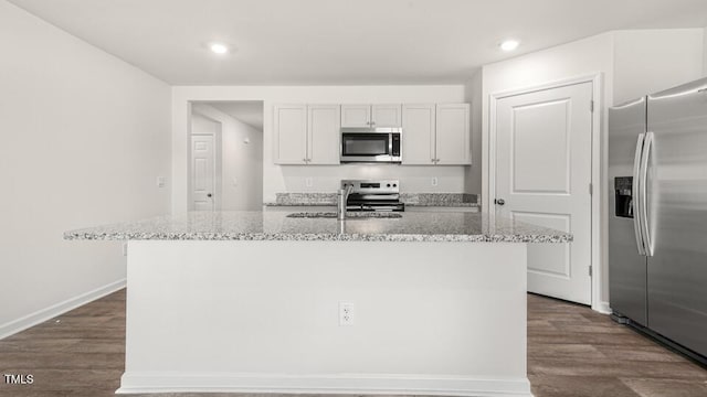 kitchen with dark wood finished floors, stainless steel appliances, light stone counters, and a sink