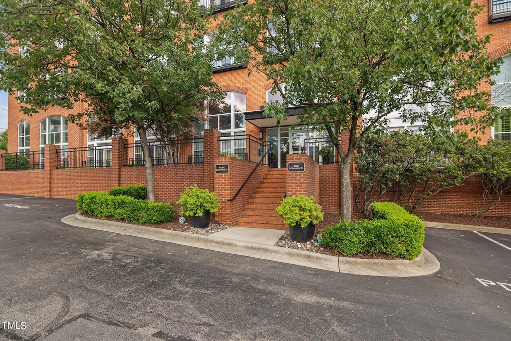 townhome / multi-family property with stairway, fence, uncovered parking, and brick siding