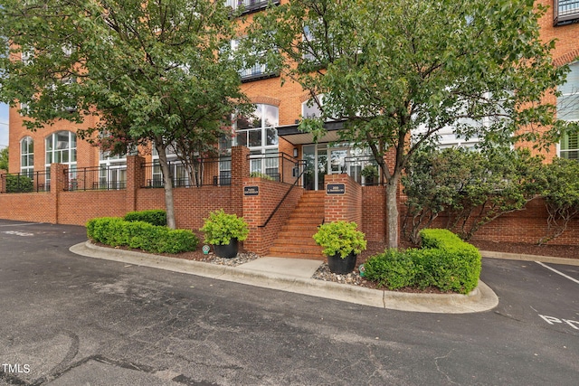 townhome / multi-family property with stairway, fence, uncovered parking, and brick siding