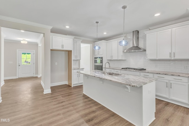 kitchen with a sink, wall chimney range hood, ornamental molding, white cabinetry, and backsplash