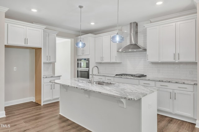 kitchen featuring a sink, stainless steel appliances, white cabinets, backsplash, and wall chimney range hood
