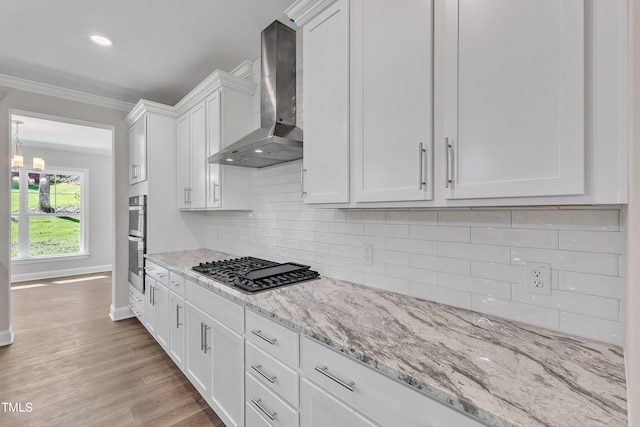 kitchen with wall chimney range hood, stainless steel appliances, ornamental molding, light wood-type flooring, and white cabinetry