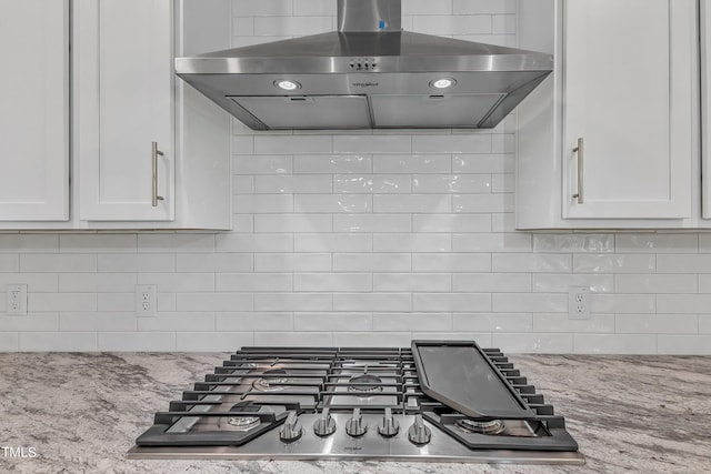 kitchen featuring stainless steel gas stovetop, ventilation hood, white cabinetry, decorative backsplash, and light stone countertops