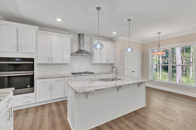 kitchen with white cabinets, wall chimney range hood, light wood finished floors, and a sink