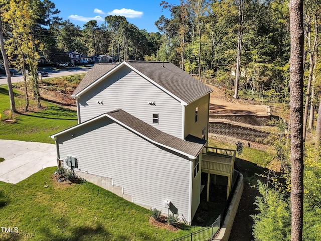 view of side of home with a shingled roof, a deck, and a lawn