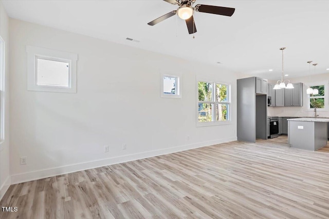 unfurnished living room featuring sink, light hardwood / wood-style flooring, a wealth of natural light, and ceiling fan with notable chandelier