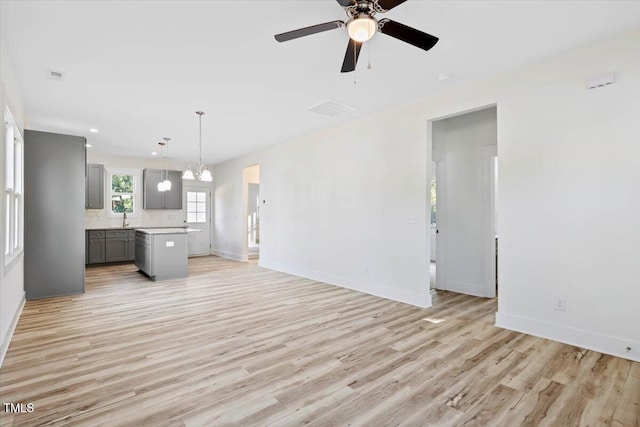 unfurnished living room with sink, ceiling fan with notable chandelier, and light wood-type flooring