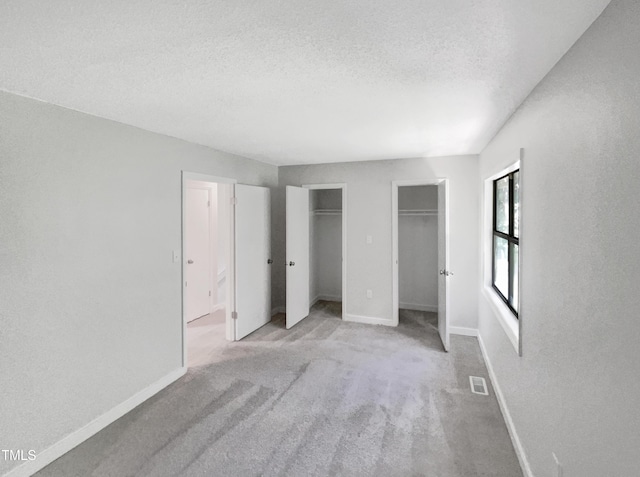 unfurnished bedroom featuring light carpet, two closets, and a textured ceiling