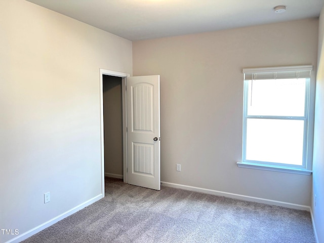 empty room featuring carpet floors, plenty of natural light, a smoke detector, and baseboards