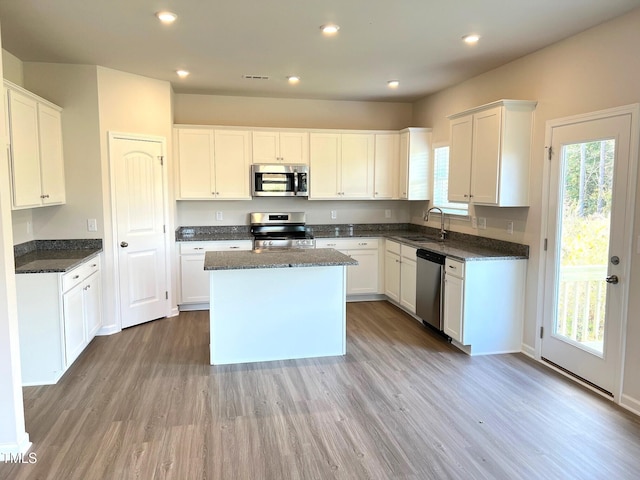 kitchen featuring stainless steel appliances, a sink, light wood-style flooring, a kitchen island, and dark stone counters