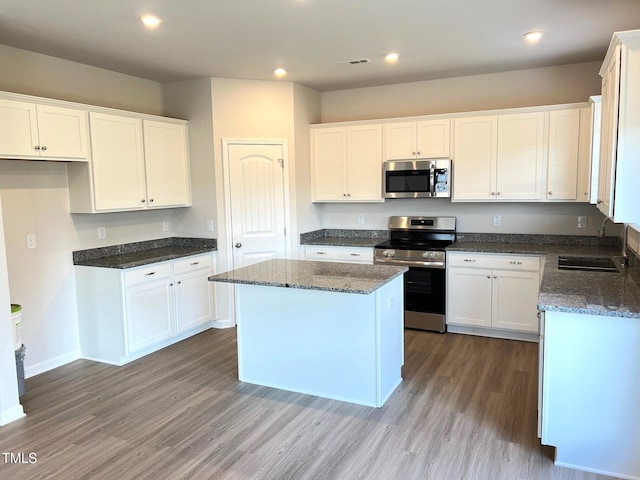 kitchen featuring stainless steel appliances, a sink, wood finished floors, white cabinetry, and recessed lighting