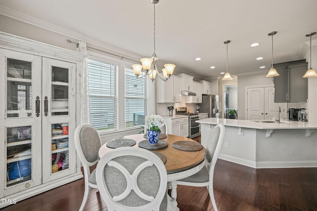 dining area with ornamental molding, a notable chandelier, dark wood-type flooring, and sink