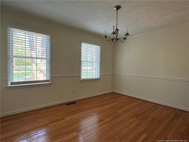 empty room featuring a textured ceiling, an inviting chandelier, and wood-type flooring