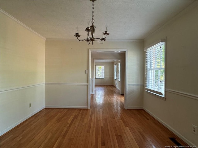 unfurnished dining area with hardwood / wood-style flooring, a chandelier, crown molding, and a textured ceiling