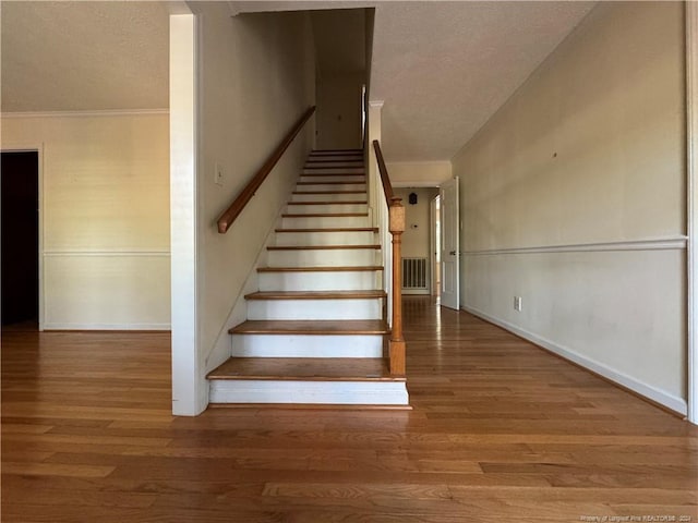 stairs featuring hardwood / wood-style floors, a textured ceiling, and ornamental molding