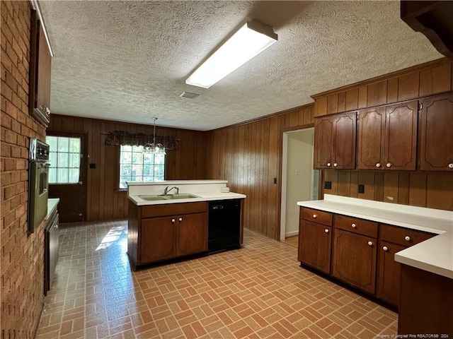 kitchen featuring decorative light fixtures, oven, sink, black dishwasher, and a kitchen island with sink