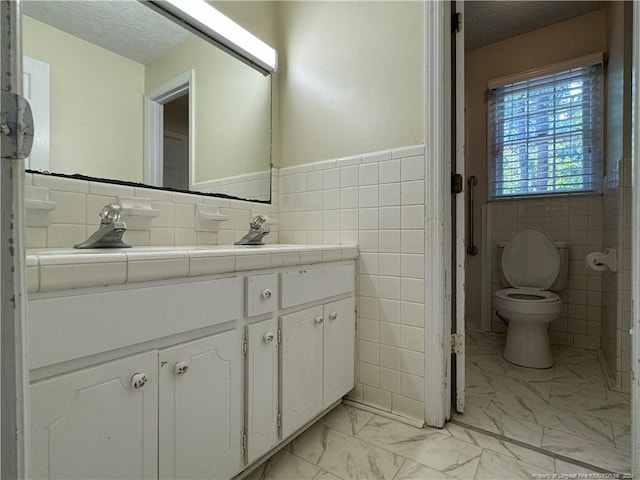 bathroom featuring a textured ceiling, vanity, tile walls, and toilet