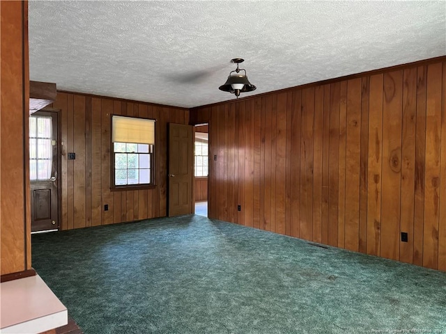 unfurnished room with a textured ceiling, dark colored carpet, and wood walls