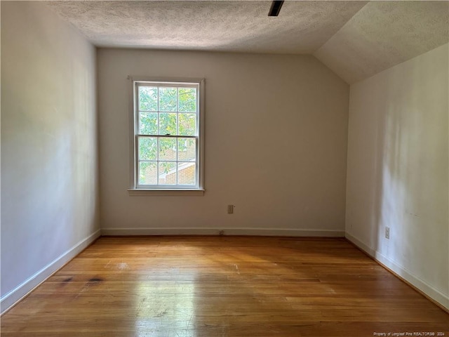 additional living space featuring a textured ceiling, vaulted ceiling, and light hardwood / wood-style flooring