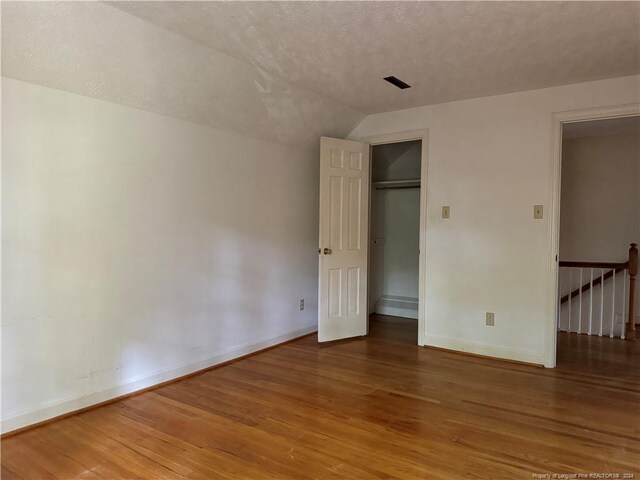 unfurnished bedroom with lofted ceiling, a closet, a textured ceiling, a spacious closet, and hardwood / wood-style floors