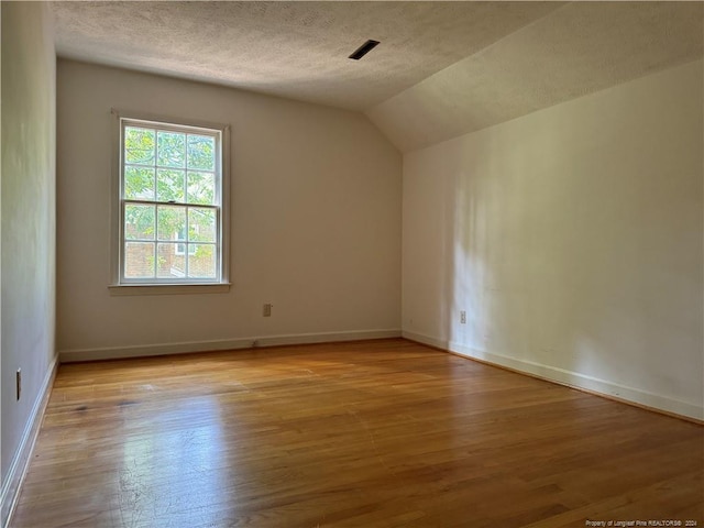 interior space featuring light wood-type flooring, vaulted ceiling, and a textured ceiling