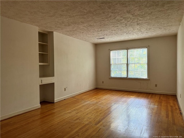 empty room with hardwood / wood-style floors, built in shelves, and a textured ceiling