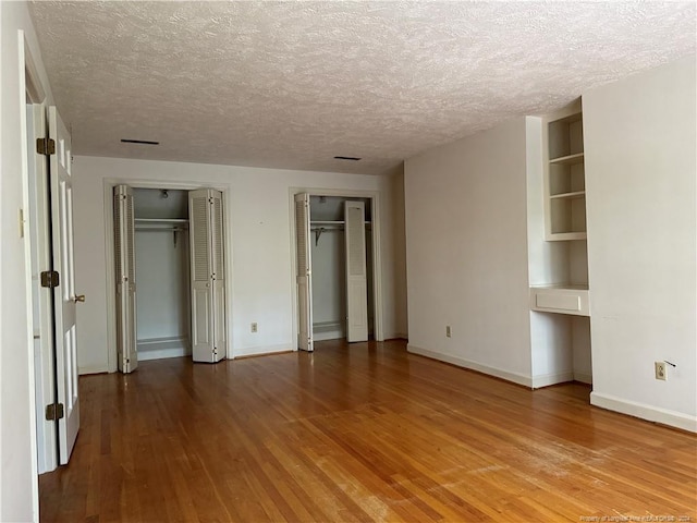 unfurnished bedroom featuring hardwood / wood-style flooring, a textured ceiling, and two closets