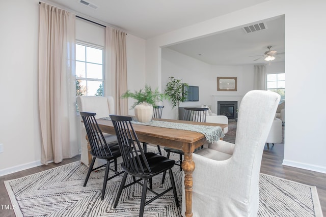 dining area featuring wood finished floors, a glass covered fireplace, visible vents, and baseboards