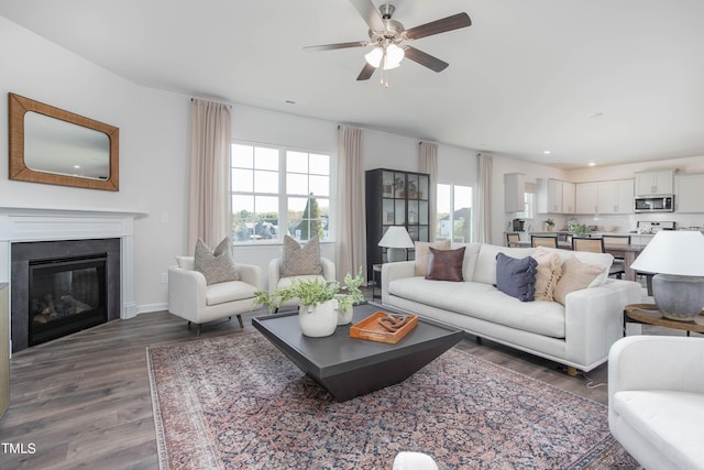 living room featuring recessed lighting, a ceiling fan, a glass covered fireplace, wood finished floors, and baseboards