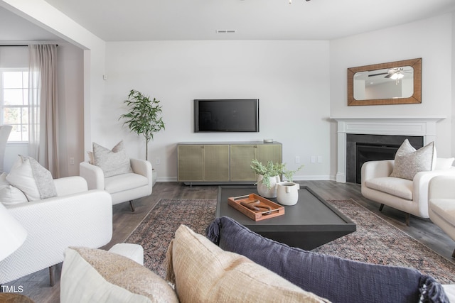 living room with a fireplace, visible vents, a ceiling fan, wood finished floors, and baseboards