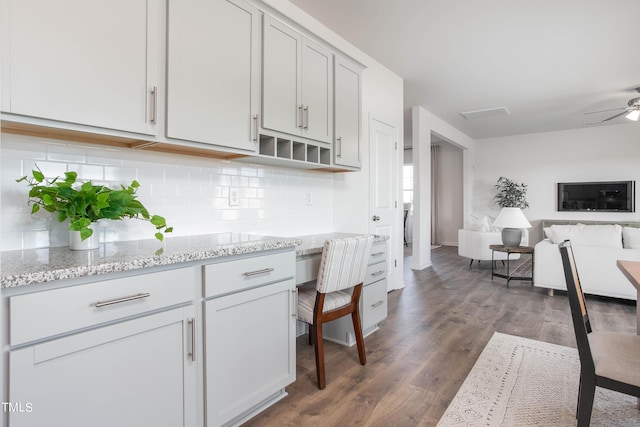 kitchen with light stone counters, dark wood finished floors, backsplash, a ceiling fan, and open floor plan