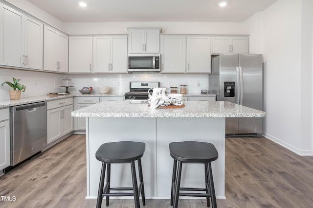 kitchen featuring a kitchen island, appliances with stainless steel finishes, a breakfast bar, wood finished floors, and backsplash