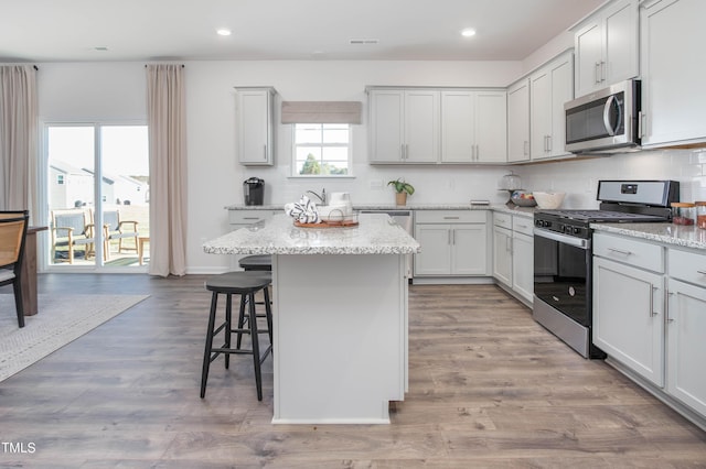 kitchen featuring a breakfast bar area, stainless steel appliances, light wood-type flooring, backsplash, and a center island