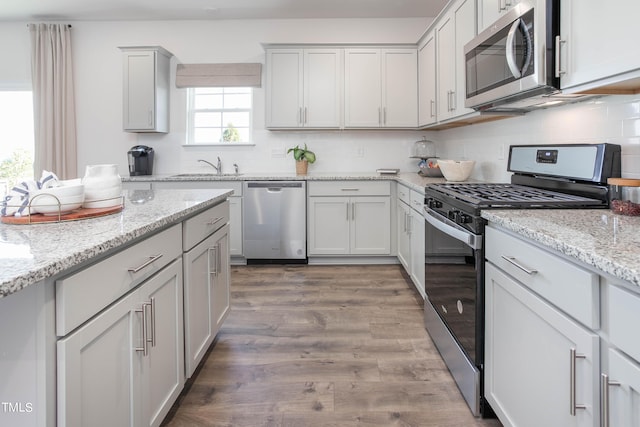 kitchen with light stone counters, backsplash, appliances with stainless steel finishes, a sink, and wood finished floors