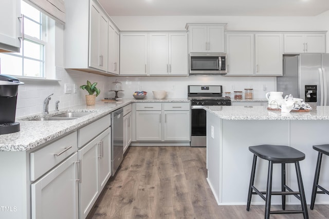 kitchen with decorative backsplash, appliances with stainless steel finishes, a breakfast bar, wood finished floors, and a sink