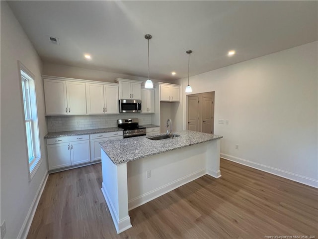 kitchen with stainless steel appliances, white cabinetry, sink, and a kitchen island with sink