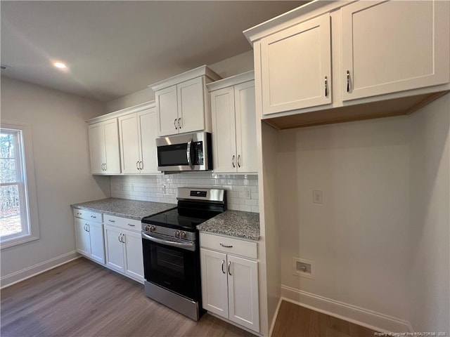 kitchen with light hardwood / wood-style flooring, appliances with stainless steel finishes, light stone counters, tasteful backsplash, and white cabinets