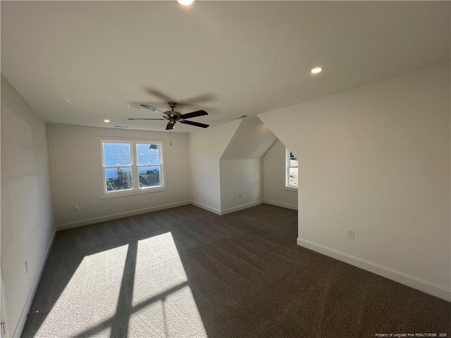 additional living space featuring ceiling fan, a healthy amount of sunlight, and dark carpet