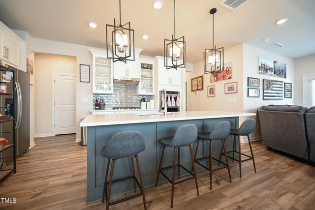 kitchen featuring hardwood / wood-style floors, a kitchen bar, tasteful backsplash, sink, and white cabinets