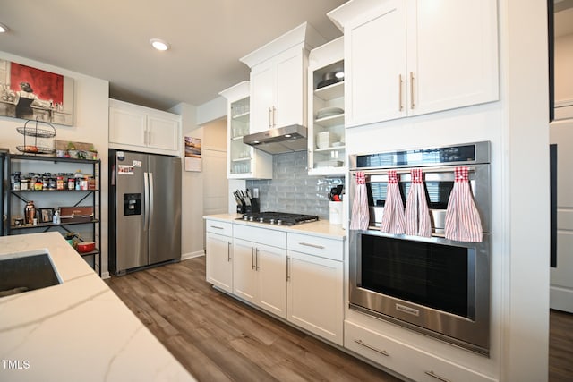 kitchen with hardwood / wood-style flooring, light stone countertops, tasteful backsplash, stainless steel appliances, and white cabinets