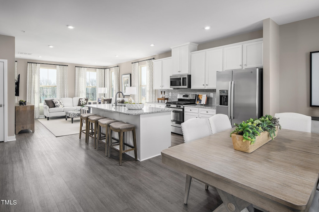 kitchen featuring a kitchen breakfast bar, an island with sink, wood-type flooring, white cabinets, and stainless steel appliances