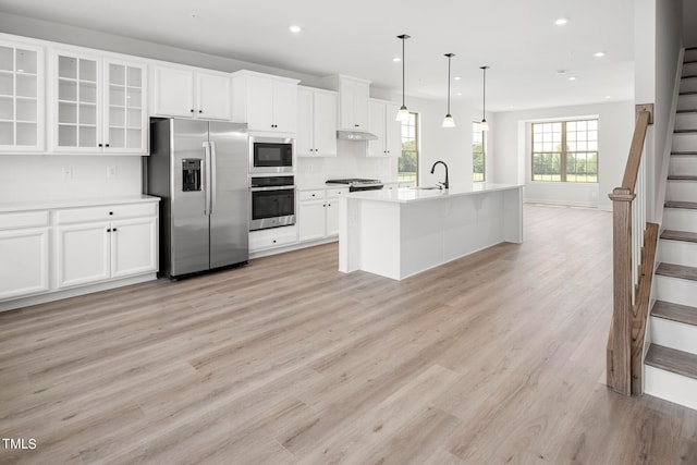 kitchen featuring light wood-type flooring, white cabinetry, sink, a center island with sink, and stainless steel appliances