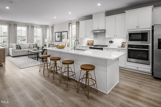 kitchen featuring stainless steel appliances, a kitchen island with sink, white cabinets, and a breakfast bar