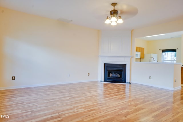 unfurnished living room featuring light hardwood / wood-style floors, a large fireplace, sink, and ceiling fan