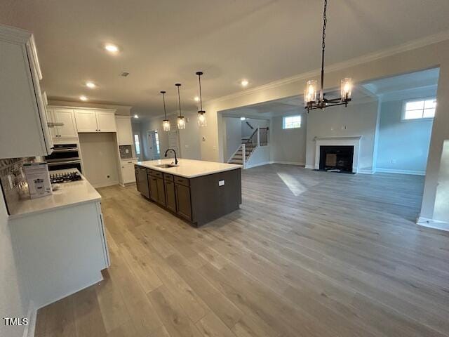 kitchen with light hardwood / wood-style flooring, crown molding, decorative light fixtures, a center island with sink, and white cabinets