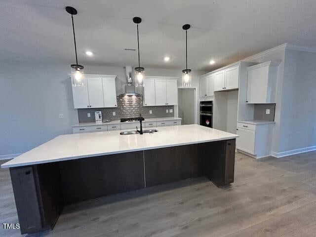 kitchen with a large island, white cabinets, wall chimney range hood, and light wood-type flooring