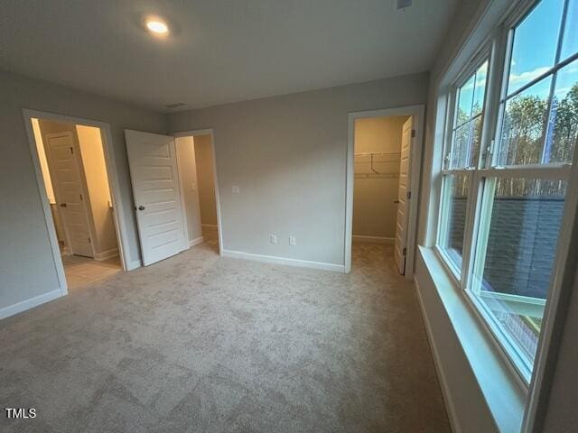 unfurnished bedroom featuring a walk in closet, light carpet, and a closet