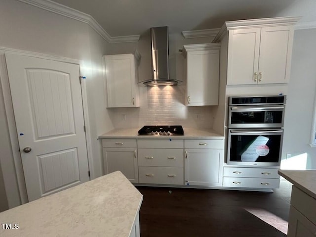 kitchen featuring white cabinetry, crown molding, wall chimney range hood, and appliances with stainless steel finishes