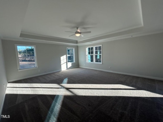 unfurnished room with a tray ceiling, ceiling fan, crown molding, and dark carpet